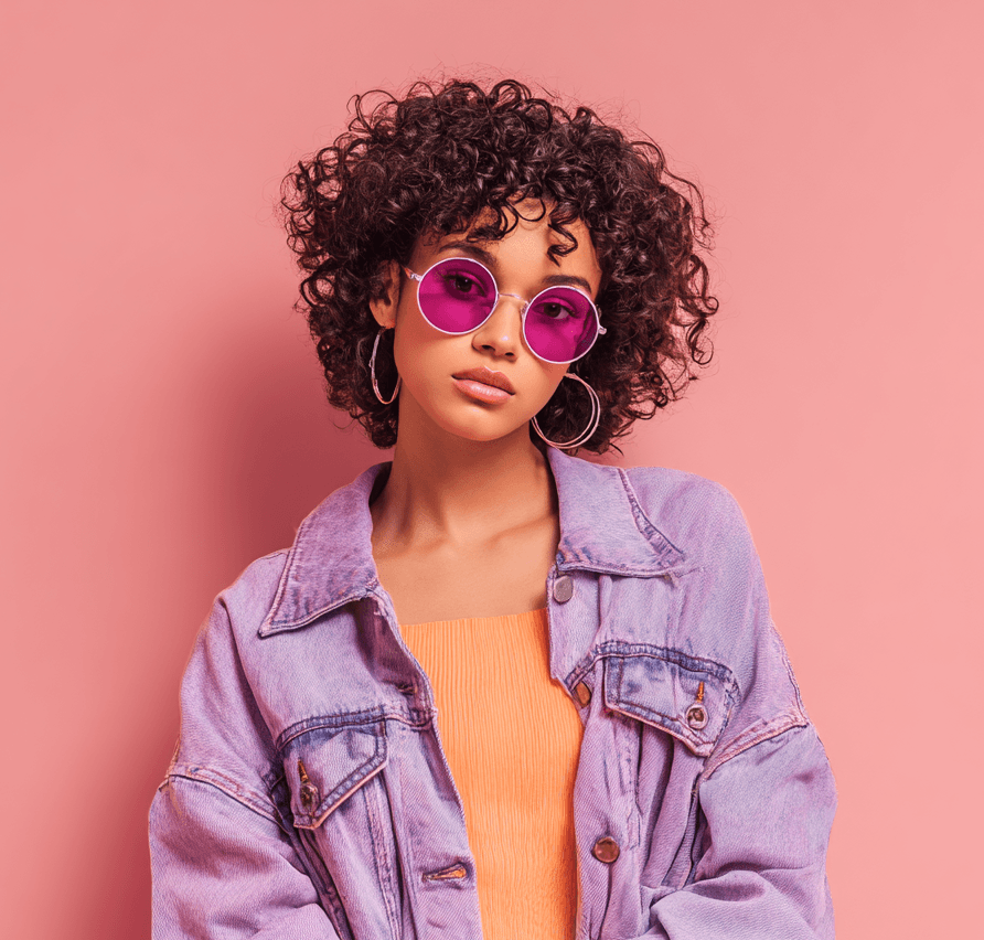Person with curly hair and purple glasses on pink background