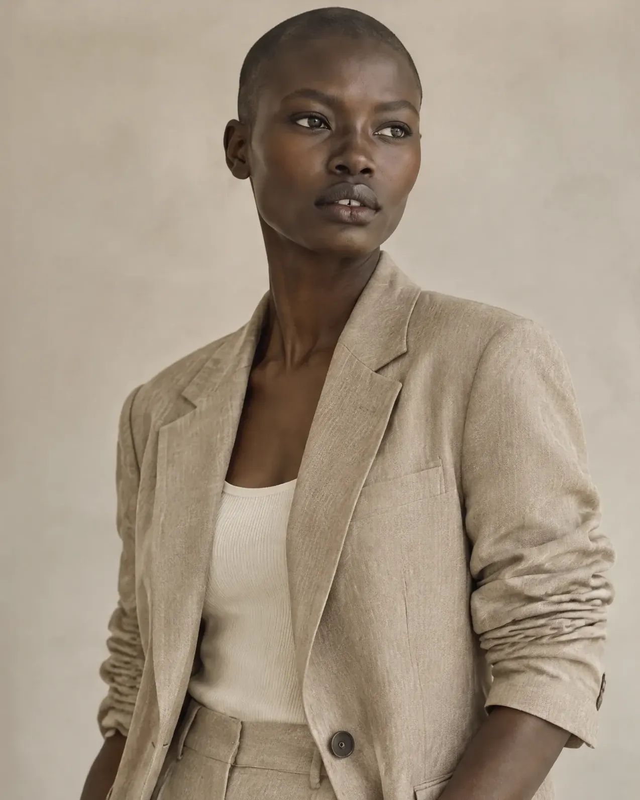 A waist-up portrait of the model in a sand-coloured linen blazer with pushed-up sleeves.