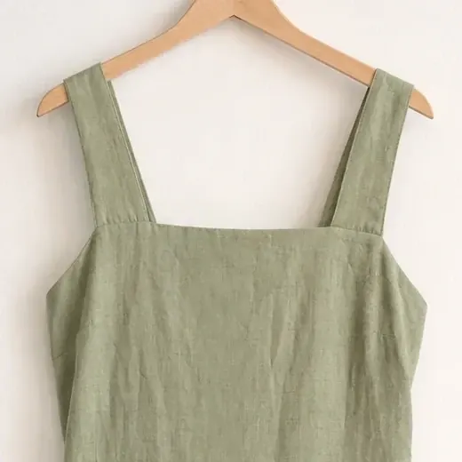 A close crop of the hanger photo: the wide straps and square neckline of a sage linen midi dress.