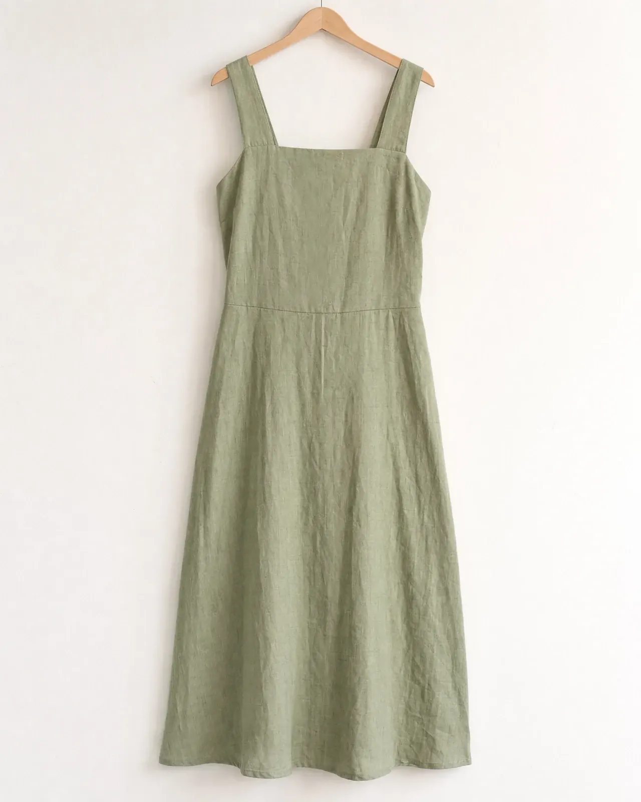 The original product photo: a sage green linen midi dress with a square neckline on a wooden hanger against a white wall.