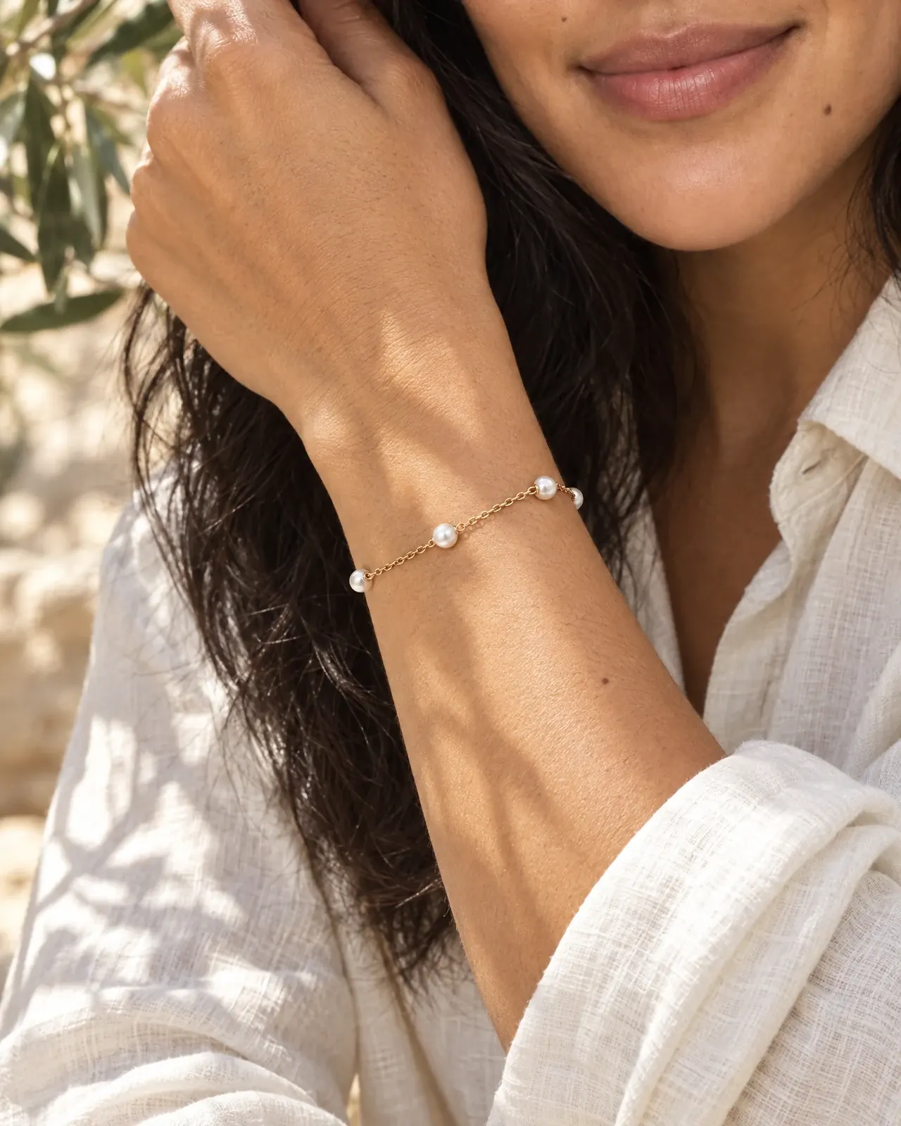 A model lifts her ivory linen sleeve to show a fine gold chain bracelet set with small pearls.