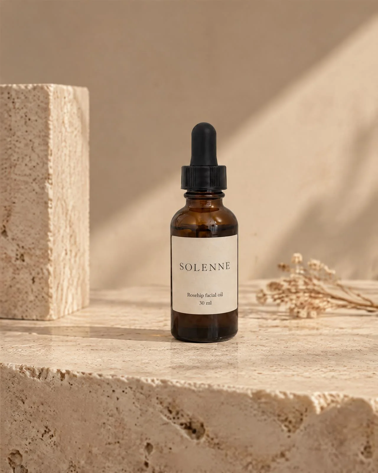 The rosehip oil bottle on a travertine block, photographed low and wide.