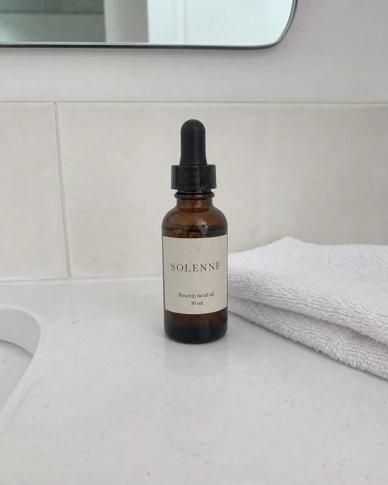 A phone photo of an amber dropper bottle of rosehip facial oil on a bathroom counter.