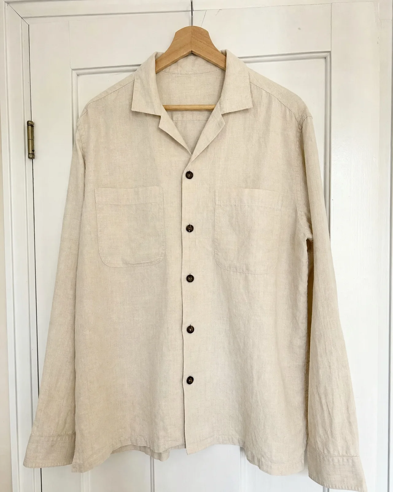 The phone photo: the linen overshirt on a wooden hanger against a white door.