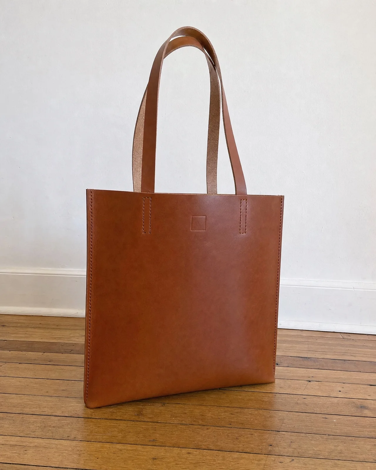 A phone photo of a cognac leather tote standing on a wooden floor.